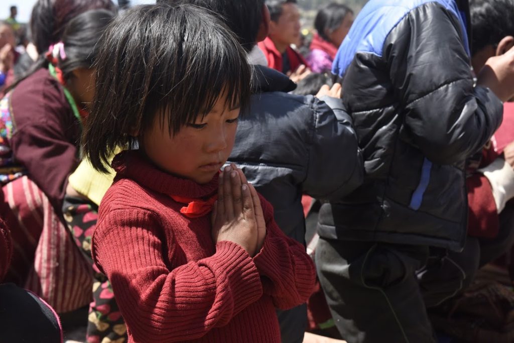 A young girl perform prayers during His Holiness' teachings. Photo @ Jamyang Tsering, DIIR