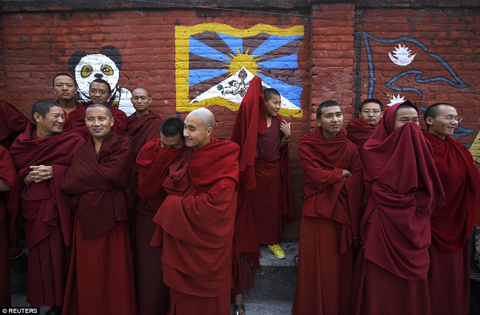 Uniform: Tibetan monks stand in front of a wall mural depicting the Tibetan flag - they clasp their cloaks around them in the chilly weather.