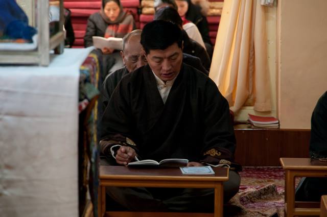 Sikyong Dr. Lobsang Sangay reading prayers from a prayer book during the service.