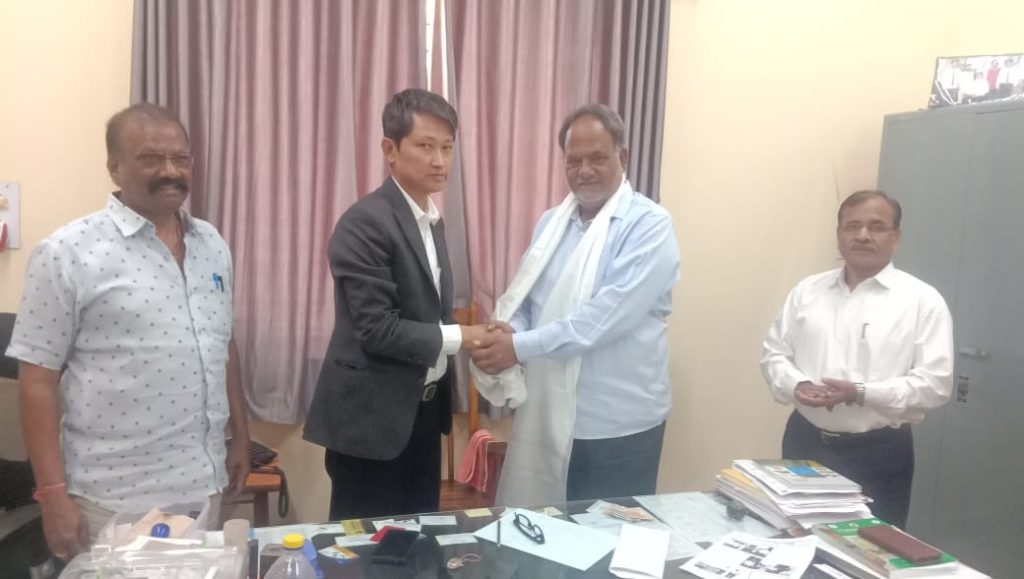 Tibetan settlement officer offers a traditional white scarf to Professor J.S. Hilli at Dharwad Agriculture University.